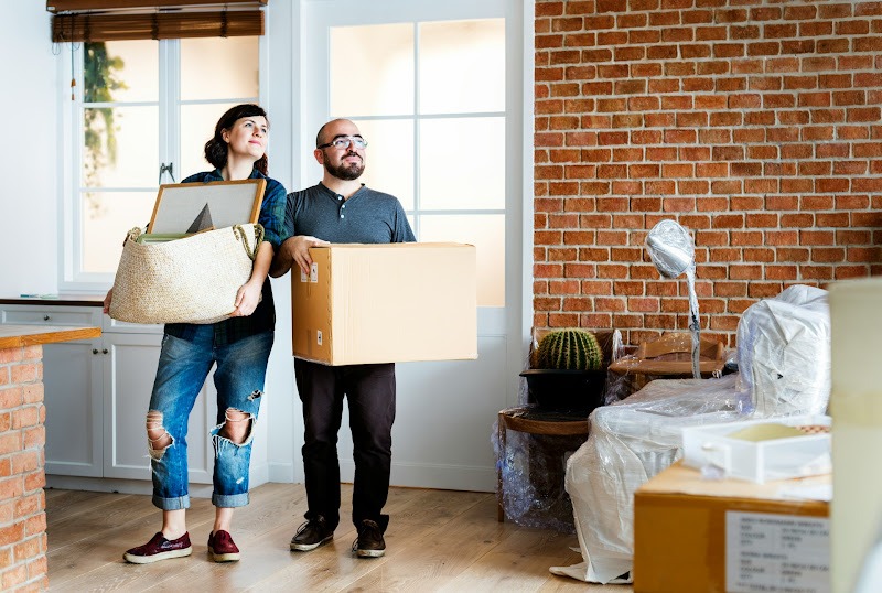 A husband and wife stand holding removal boxes, saying goodbye to their old London home